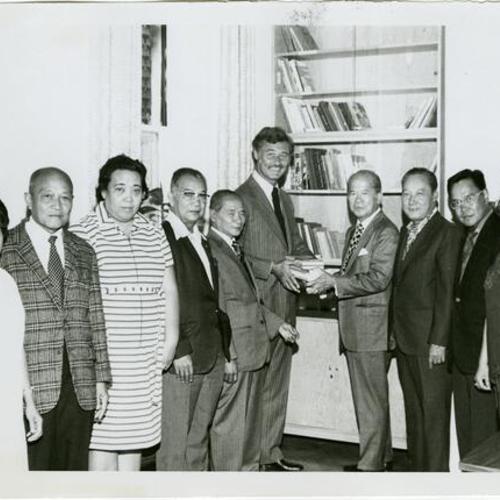 [George Moscone at a Filipino event holding a stack of books]