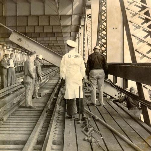 [Group of Bay Bridge and Key System workmen surveying damage caused by a giant crane, atop a barge, which slammed against the lower deck of the San Francisco-Oakland Bay Bridge]