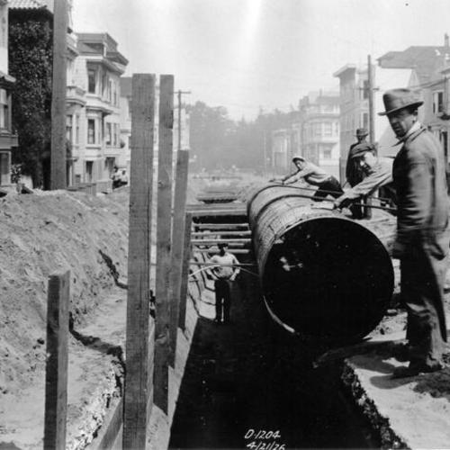 [Construction workers lowering pipe into trench along Sixth Avenue and Irving Street]