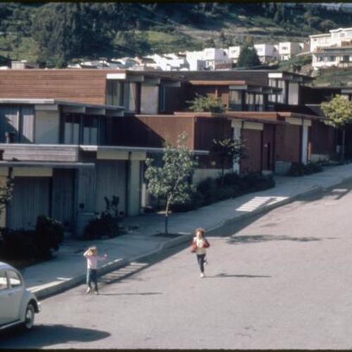 [Children run on a Diamond Heights street, homes traverse the hillside in the background]