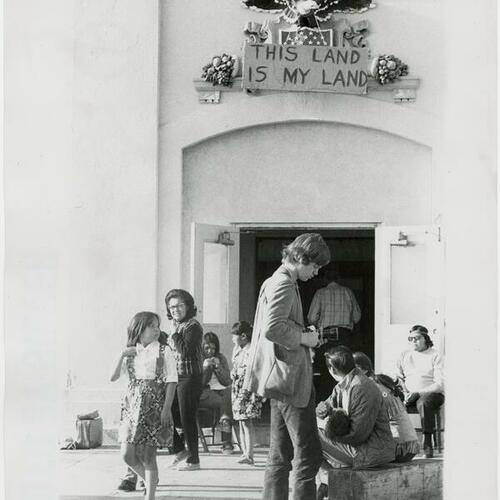 People outside the Administration Building on Alcatraz with a "This land is my land" sign hanging over the doors
