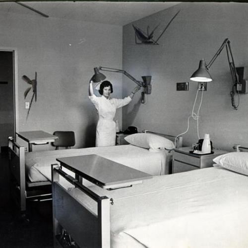 [Nurse Chris Henderson demonstrating an adjustable lamp in a two bed ward at French Hospital]