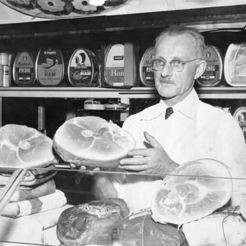 [George Freeze displaying a ham at a delicatessen in the Crystal Palace Market]