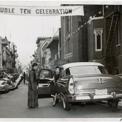 [Chong Lee holding the door of a 1956 Dodge for Helen Lee during the lull of the 'Double Ten' festival]