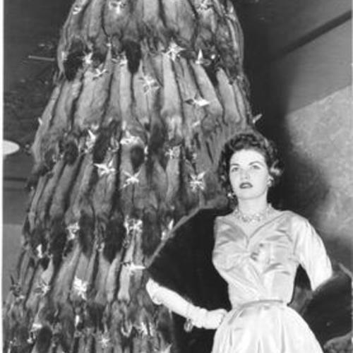 [Dixie Massey standing next to a sable skin Christmas tree at I. Magnin]
