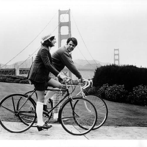 [Man and woman bicycling and Golden Gate Bridge is shown in the background]