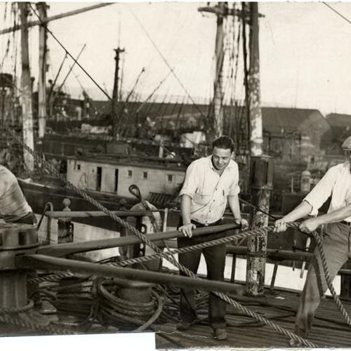 [Crew members manning the capstan on the sailing ship "Pacific Queen" (also known as the "Balclutha")]