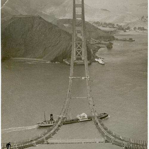 [Ship passing under catwalk construction of Golden Gate Bridge]