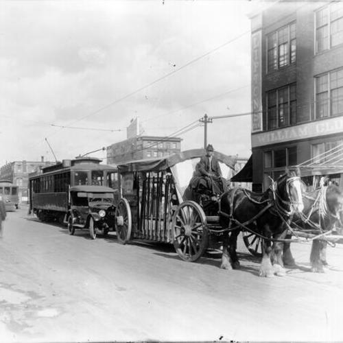 [Horse drawn wagon leading automobile and electric trolley car procession]