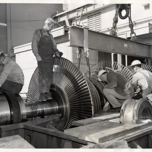 [Workmen easing a steam turbine rotor into position at a new power plant in the Hunters Point district]