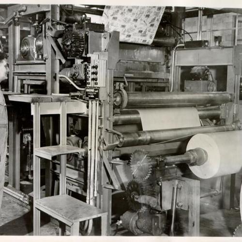 [Unidentified employee standing near a laminating machine at the Andre Paper Box Company]