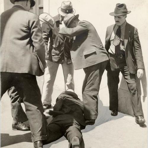 [Group of men standing over another man who was wounded during longshoremen's strike]