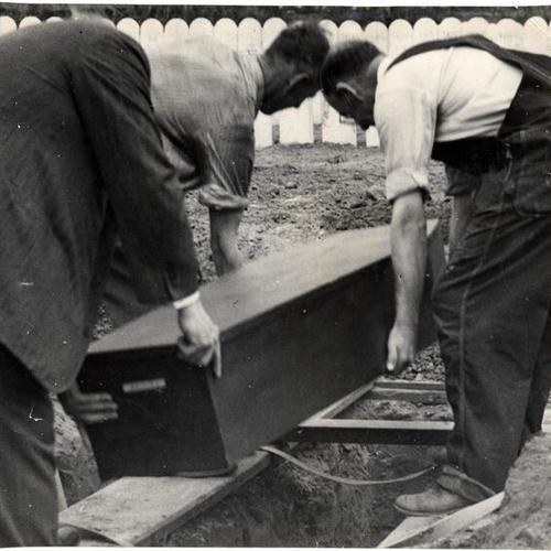 [Casket containing Alexander Allison being lowered into a plot in Potters Field at Colma Cemetery]