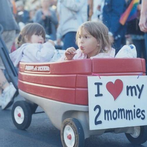 [Children of lesbian parents sitting in a Radio Flyer trailer with a sign in 2007 Pink Saturday Dyke March on Dolores and 18th Streets]