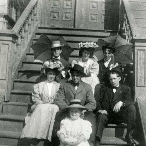 [Portrait of seven family members sitting on steps of house on Treat Street]