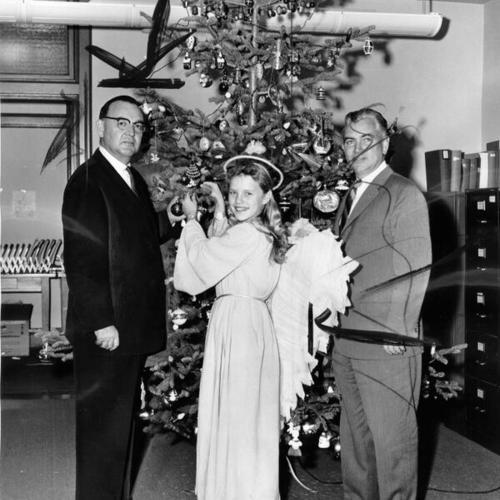 [Governor-elect Edmund G. (Pat) Brown and 12-year-old Kathy Roche, Guardmen's "Christmas Angel," place final ornaments on the State Building's Christmas tree]