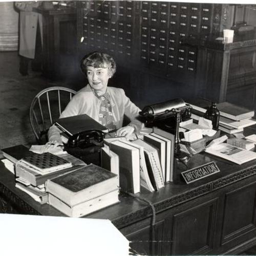[Librarian Helen D. Livingston working at the information desk at the Main Library]