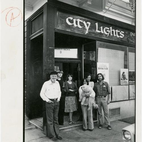 [Lawrence Ferlinghetti, Pamela Mosher, Nancy Peters, Julie Ferlinghetti, Stella Levy and Craig Bradley standing in front of City Lights publishing and editorial offices at 1562 Grant Ave.]