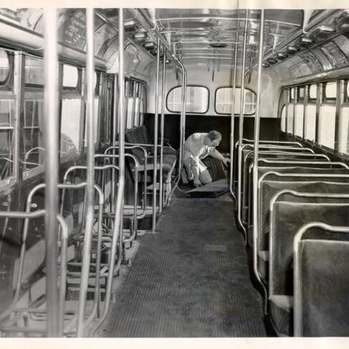 [Municipal Railway employee Charles McGuire inspecting damaged seats at the back of a Muni bus]