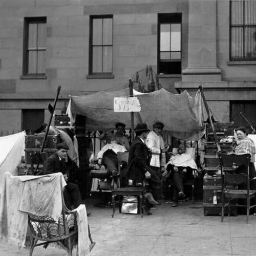 [Two men receiving shaves at a makeshift barber shop in front of the Old Mint at 5th & Mission, 1906]