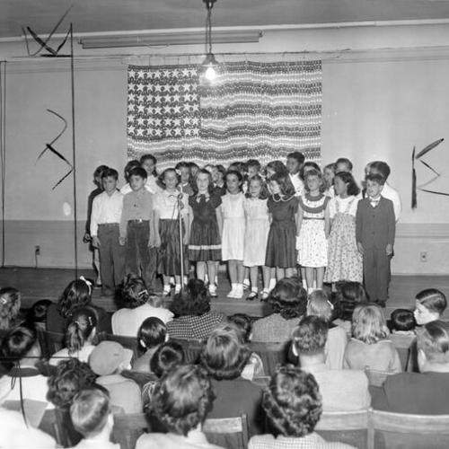[Children on stage before an audience of parents at Sarah B. Cooper School]