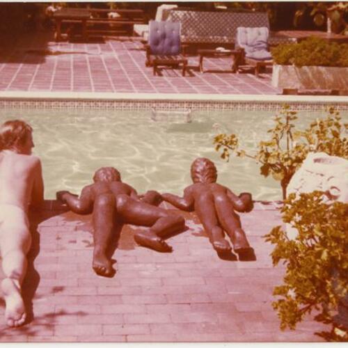 Nude person laying poolside next to statues at Rock Hudson's home, The Castle, Beverly Hills
