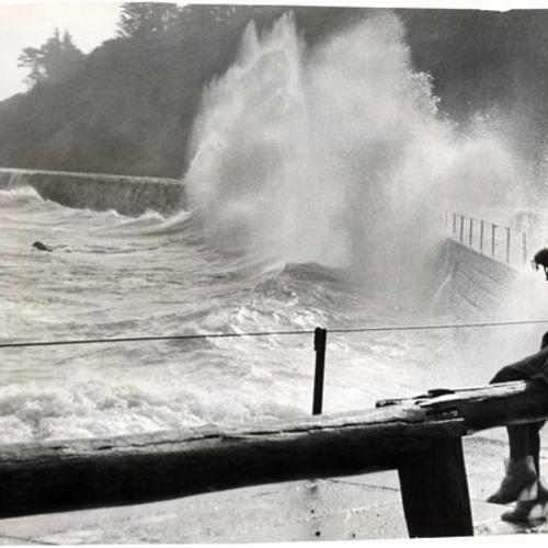 [Unidentified woman watching waves crash against the sea wall at Fort Point]