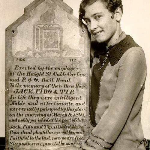 [Vera Stevens holding a plaque erected by employees of the Haight Street Cable Car Line in memory of their three dogs, Jack, Fido and Tip]