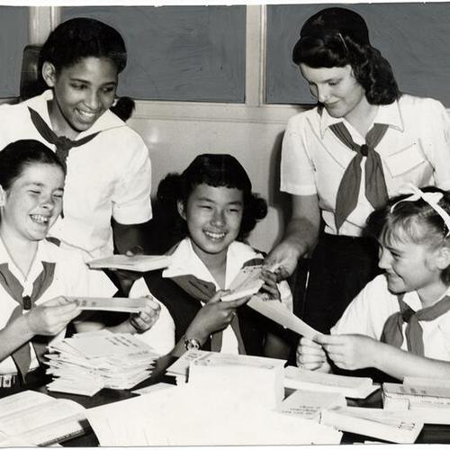 [Camp Fire Girls Ina Flemming, Merlene Siegner (standing), Joyce Prisk, Joyce Hirota and Theda Nielsen (sitting) filling envelopes at the California Council of Civic Unity]