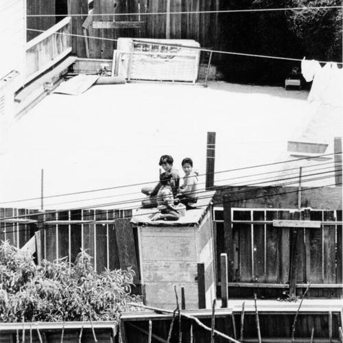 [View from 624 Ashbury Street of three children sitting on top of a wooden structure in the backyard of 1900 Haight Street]