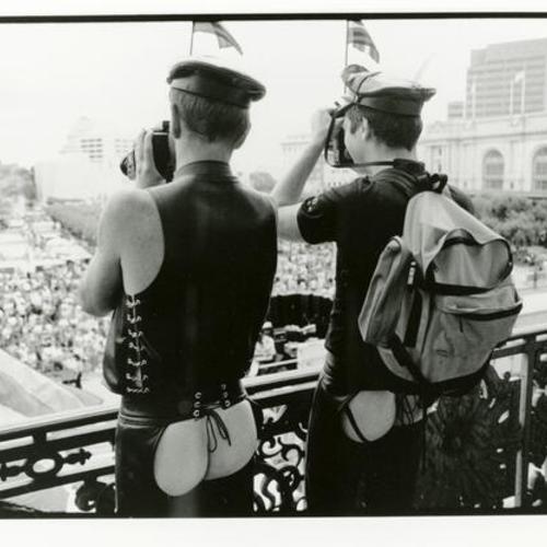 [Two men in chaps taking pictures from the balcony of the mayor's office during San Francisco Gay Pride Day]