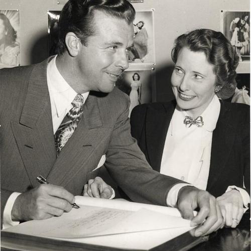 [Dick Powell at the Stage Door Canteen posing with Mrs. Hanan, vice chairman for the canteen's entertainment committee]