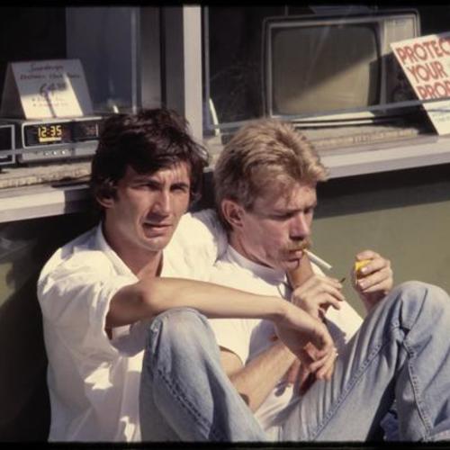 Two people sitting in front of storefront smoking