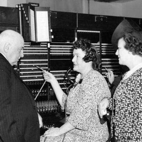 [Mayor Angelo J. Rossi standing with telephone operators Mrs. Josephine R. Black and Mrs. C. E. Brosiua]