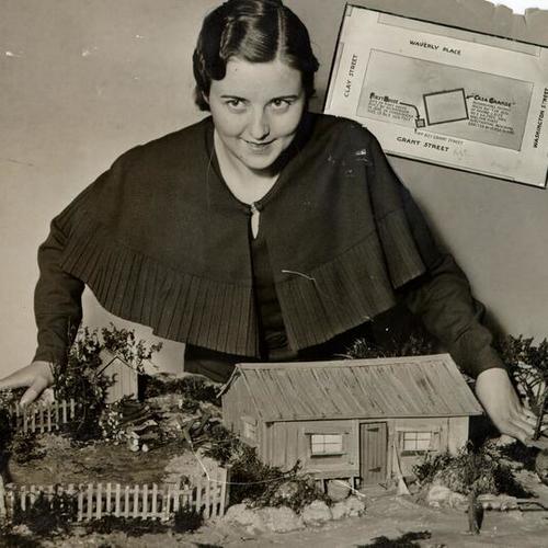 [Thelma Dakin standing next to the model of the first home built in San Francisco by architect William A. Richardson]