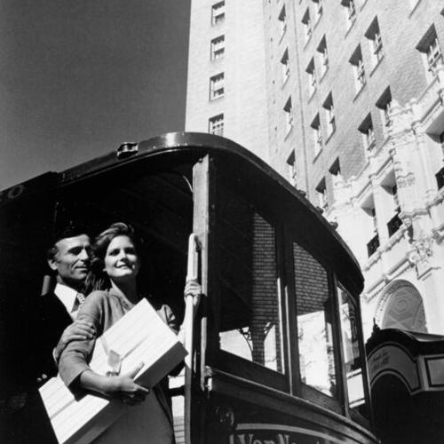 [Two unidentified people on a cable car in front of the Mark Hopkins Hotel]
