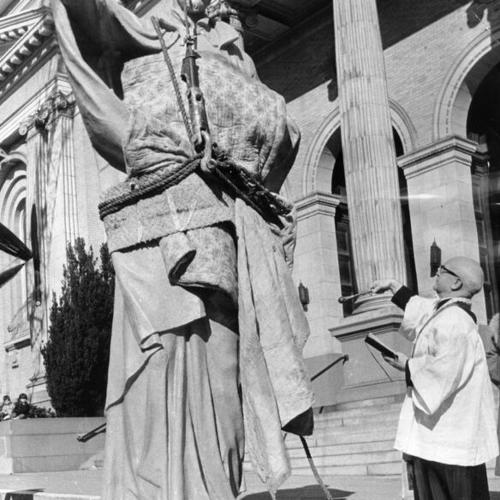 [Rev. Thomas J. Cosgrave sprinkling holy water on a statue of St. Ignatius at St. Ignatius Church]