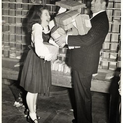 [Postmaster Bill McCarthy with comedienne Marcy McGuire encouraging San Franciscans to shop, wrap and mail their Christmas packages early]