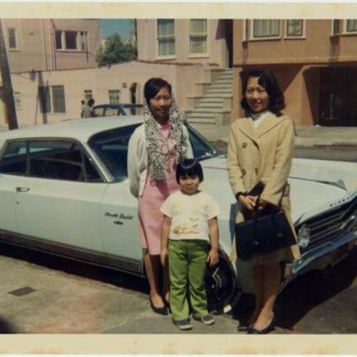 [Juanita, Francis, Veronica, posing with neighbor's Oldsmobile outside of family house]