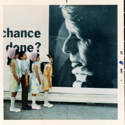 [Maria, Tony, Sylvia, Zenaida standing in front of a Bobby Kennedy campaign poster]