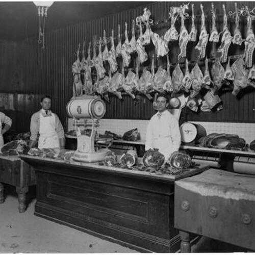 Three butchers standing behind meat counter at butcher shop