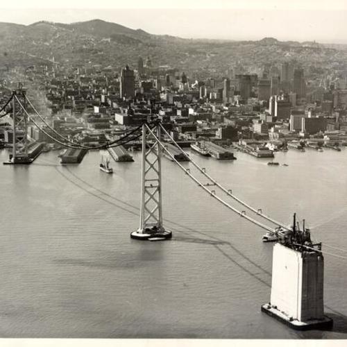 [Aerial view of catwalk of San Francisco-Oakland Bay Bridge stretched out over the bay to San Francisco during construction]