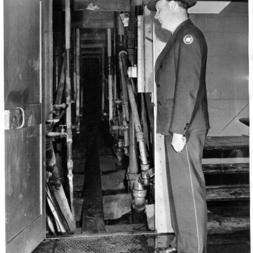 [Unidentified Alcatraz prison guard standing next to a utility corridor in Cell Block C where the bodies of three convicts who were killed in an escape attempt were found]