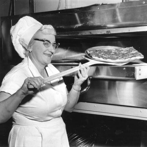 [Frances Ketchum taking a pizza out of an oven at a pizza stand in the Crystal Palace Market]