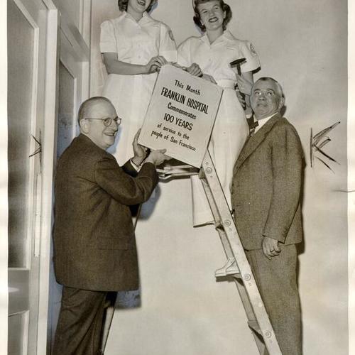 [Franklin Hospital officials and nurses hanging a poster to commemorate the 100th anniversary of the hospital]