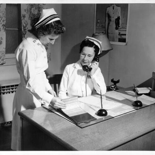 [Lieutenant Commander Laura M. Cobb, chief nurse at Treasure Island Navy Hospital, consulting with an assistant]