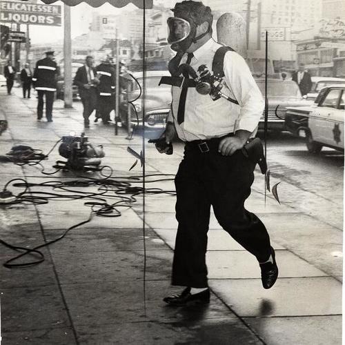 [Officer John O'Connor wearing a gas mask and carrying a gun in his right hand]