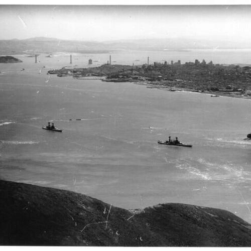 [View of ships passing by partially constructed Golden Gate Bridge, with partially constructed Bay Bridge visible in background]