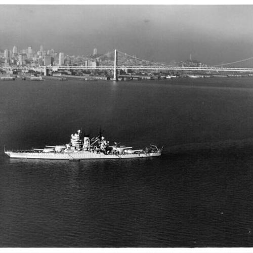[U.S. Navy battleship sails through San Francisco Bay with Bay Bridge and San Francisco skyline in background]