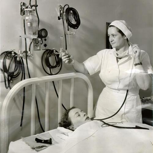 [Anaesthetist Cecelia Davis and student nurse Jane Van Eppuen demonstrating equipment available to patients in the surgical recovery room at Franklin Hospital]